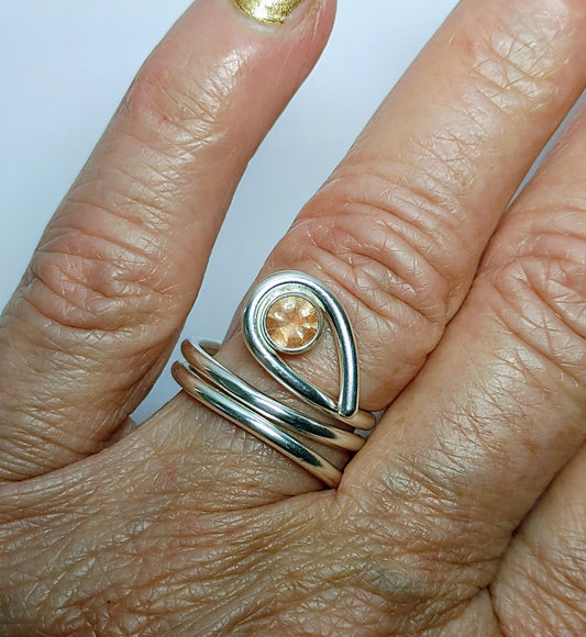 Close-up of a hand wearing two silver rings with a teardrop-shaped gemstone on a light background