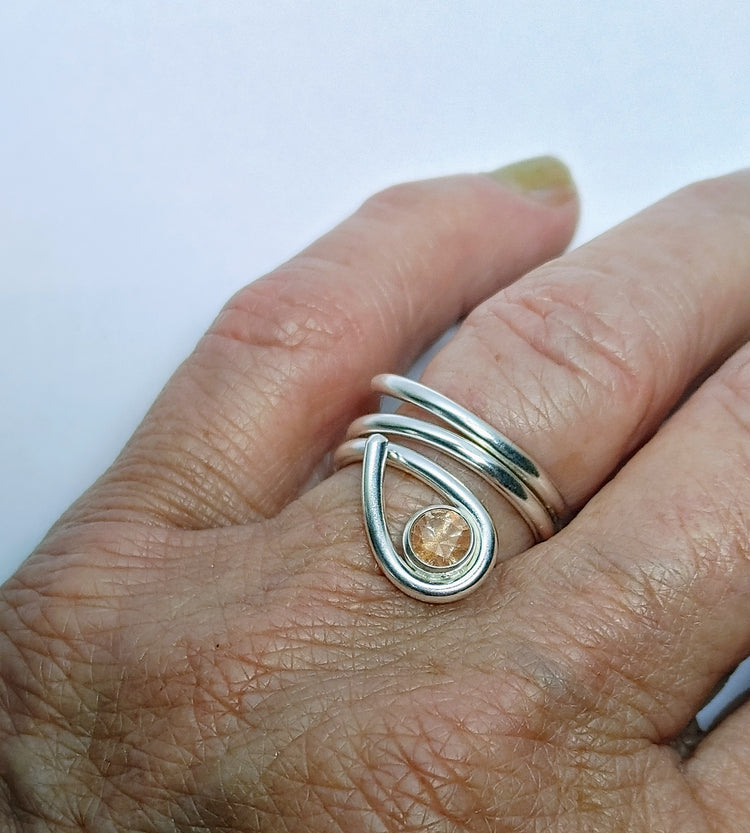 Silver ring with a teardrop design and bezel set sunstone on a hand against a white background