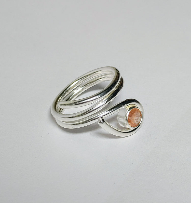 Silver ring with a peach schiller sunstone on a light gray background