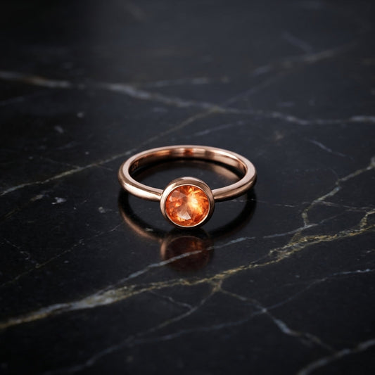 Overhead artistic shot of a rose gold sunstone ring on dark marble, emphasizing its warm glow, micro-texture, and modern elegance under soft lighting.