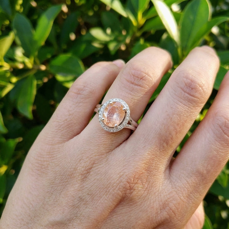 Close-up of the Sunstone Halo Ring on a finger outdoors, capturing the shimmer of the sunstone and halo diamonds in natural light.