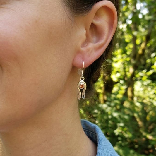 Close-up of a female model wearing delicate silver dangle earrings with peach Oregon Sunstone in natural sunlight.