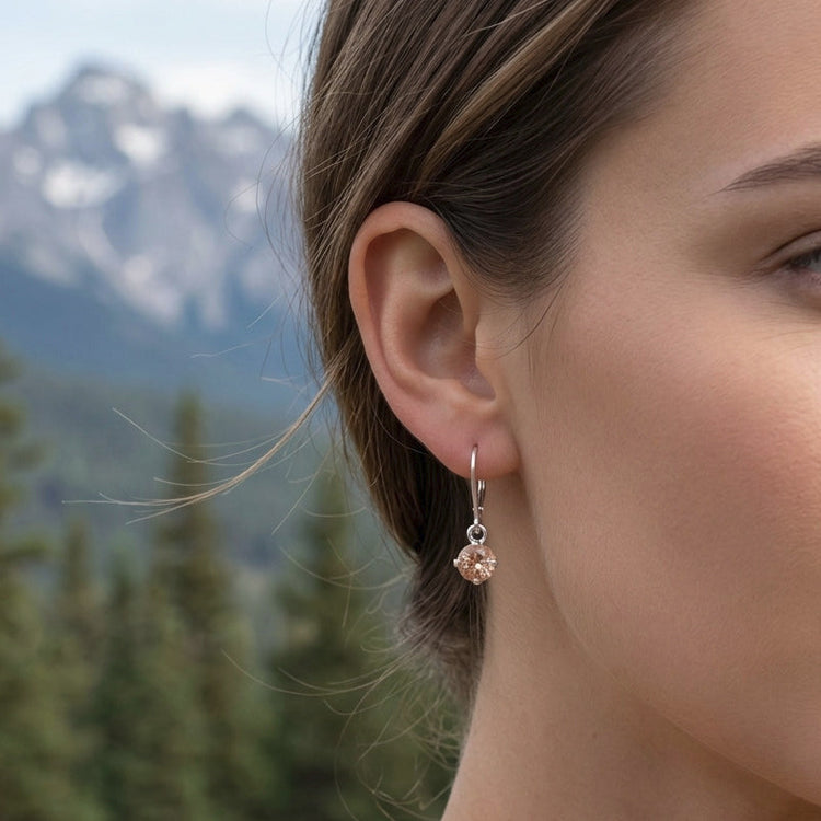 Close-up of a delicate silver sunstone dangle ring on a hand with a natural outdoor background and pine trees, highlighting gemstone clarity and fine details.