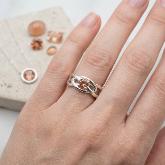 Close-up of a small silver Celtic Sunstone Ring with a 4.5mm Oregon Sunstone, showcasing warm peach hues on an elegant hand with refined skin.