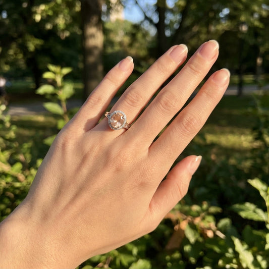 Hand wearing the Sunstone Halo Ring on the third finger with a park background, showcasing the ring's craftsmanship and delicate size.