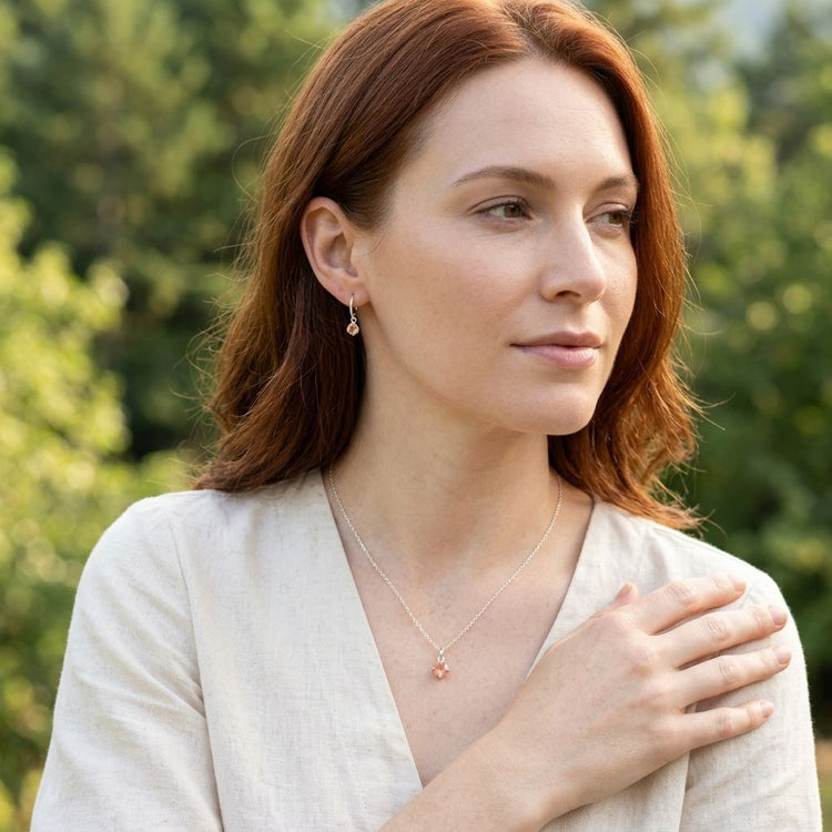Female model wearing sterling silver hoop earrings with peach-hued Oregon Sunstone dangles, outdoors with natural scenery and relaxed pose.