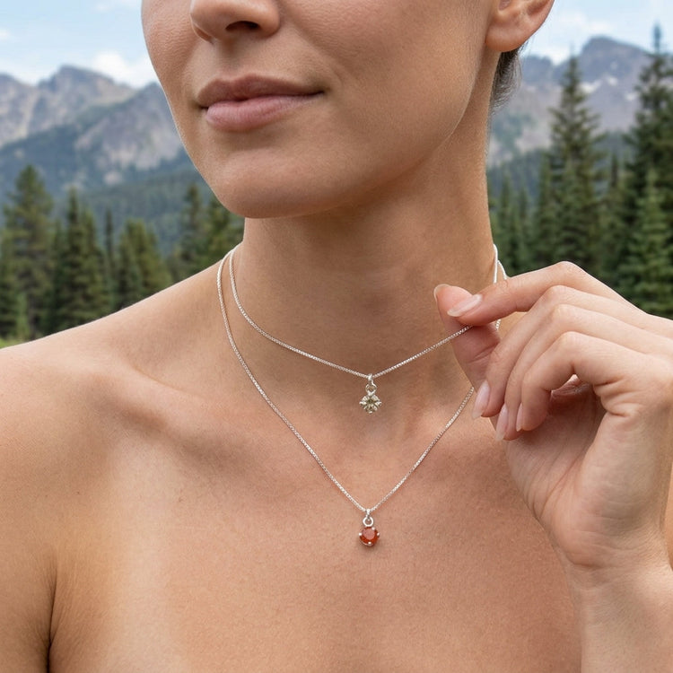 Full-body outdoor shot of a stylish model showcasing a small silver Sunstone pendant necklace on a light chain amid a mountain landscape.