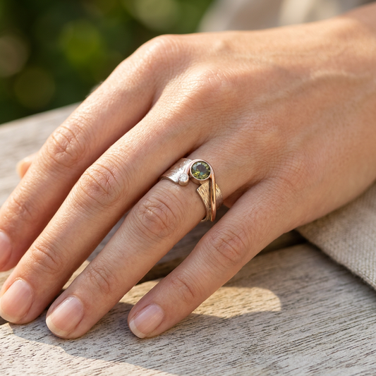 Close-up of a 14K gold ring with vibrant green Oregon Sunstone on a manicured hand outdoors, accentuating the ring's texture and gemstone's luster.