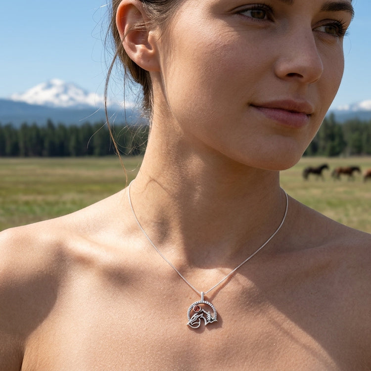 Model holding a small sterling silver horse pendant with Oregon Sunstone against her hand in a natural outdoor setting, highlighting subtle size and details.