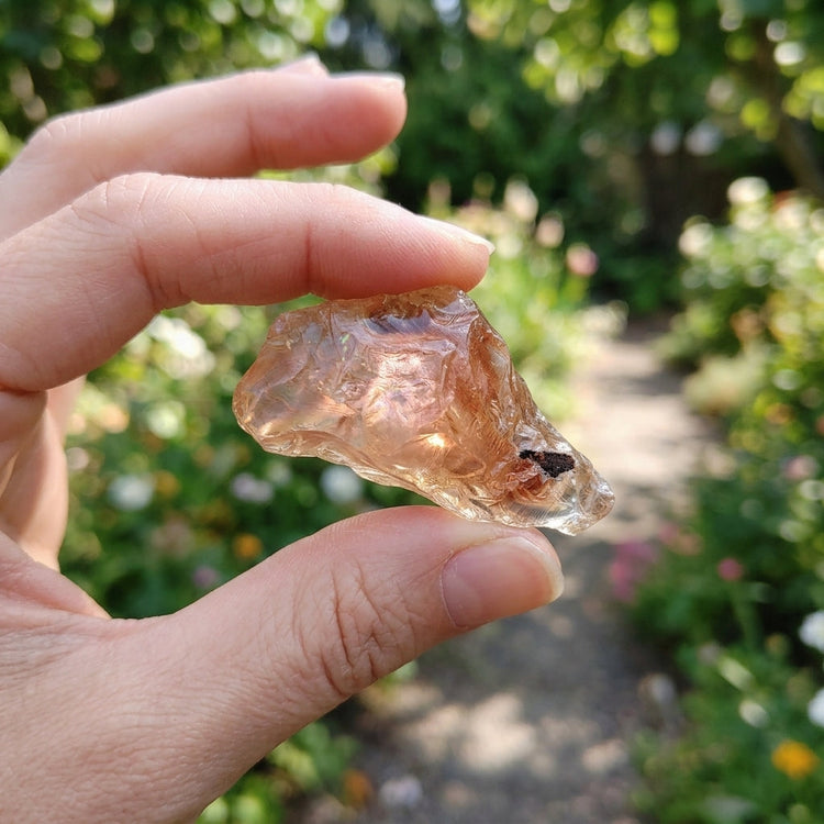 Natural outdoor scene with model showcasing Oregon Sunstone ring, bright lighting emphasizing vibrant orange-red shimmer and texture.