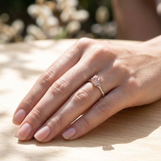 Full view of a manicured hand resting on a light wooden surface outdoors, showcasing a white gold Oregon Sunstone 'Starburst' engagement ring.