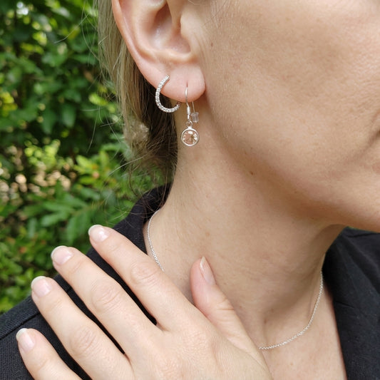 Detailed shot of a female model in a green outdoor setting showcasing her neckline with silver earrings and a petite necklace.