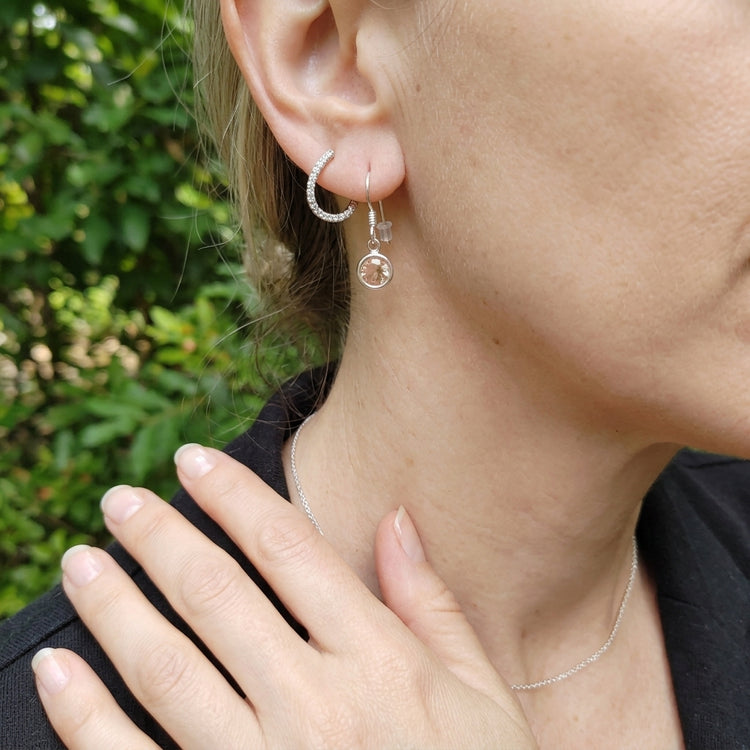 Detailed shot of a female model in a green outdoor setting showcasing her neckline with silver earrings and a petite necklace.