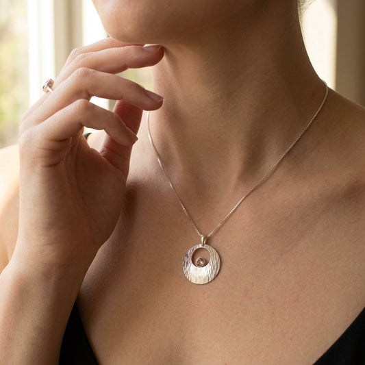 Full-body of a model showcasing a small silver Galilean Moon pendant necklace with Oregon Sunstone, elegant and delicately resting on the collarbone.