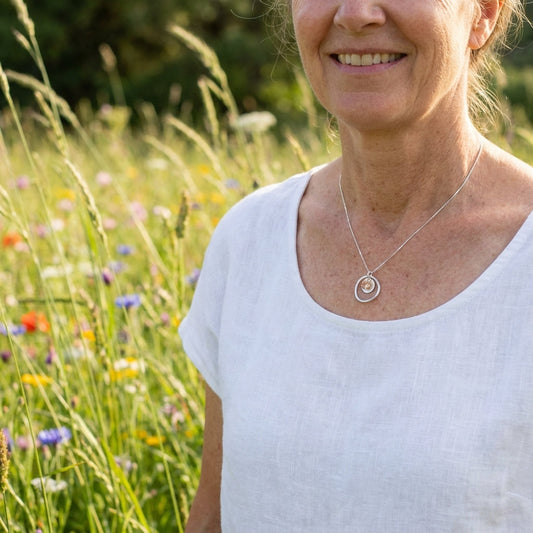 Model wearing Sunstar necklace in an outdoor setting with tall grass and wildflowers, emphasizing its delicate size and natural beauty.