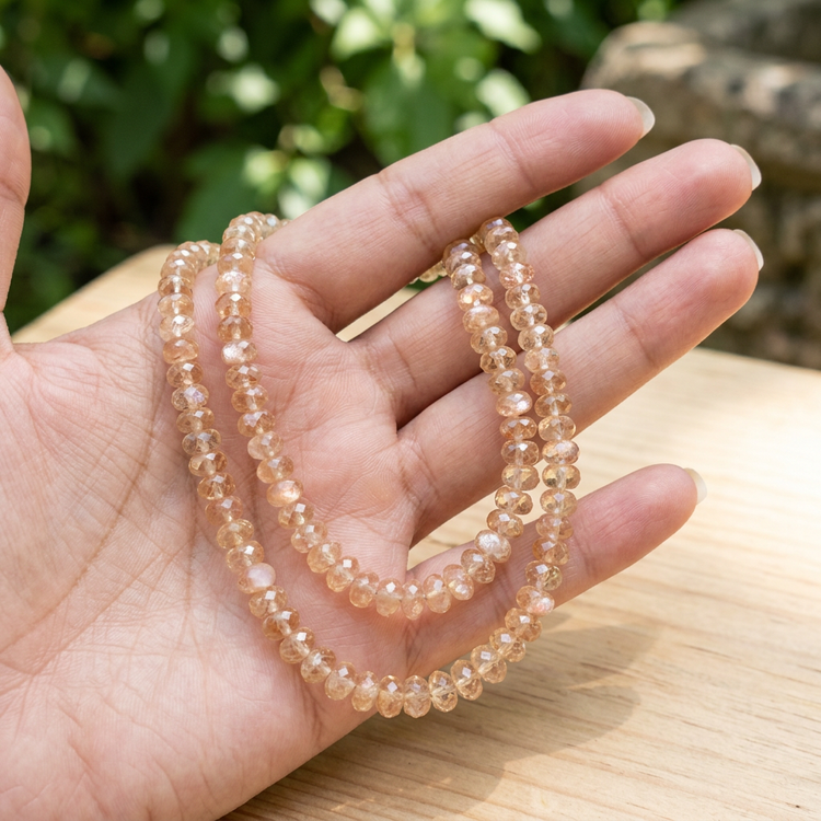 Two Oregon Sunstone bead strands loosely arranged on a hand outdoors, highlighting their subtle size variation and harmonious champagne and pink hues.