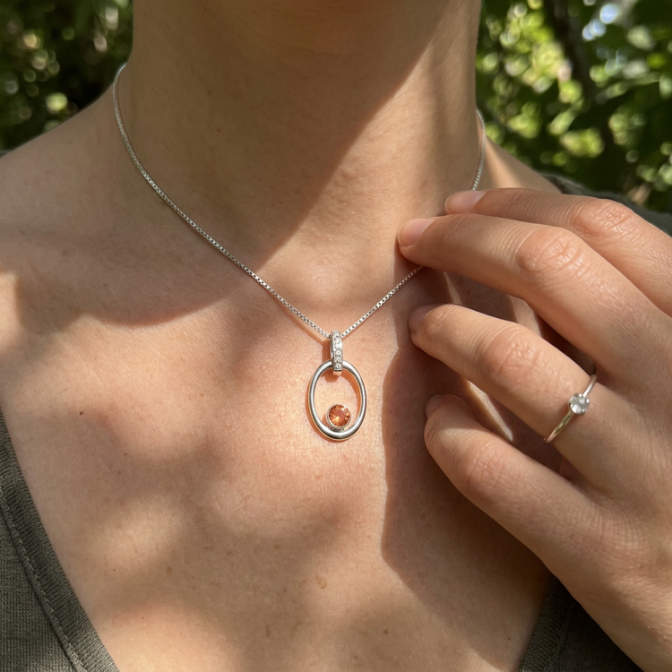 Female model outdoors displaying a delicate Oregon Sunstone pendant with ice diamonds on a silver chain, surrounded by greenery.