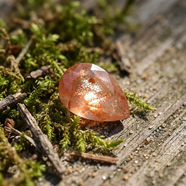 Overhead view of peach Schiller sunstone nestled among moss, twigs, and sand on rustic wood, illuminated by soft morning sunlight highlighting its intrinsic beauty.