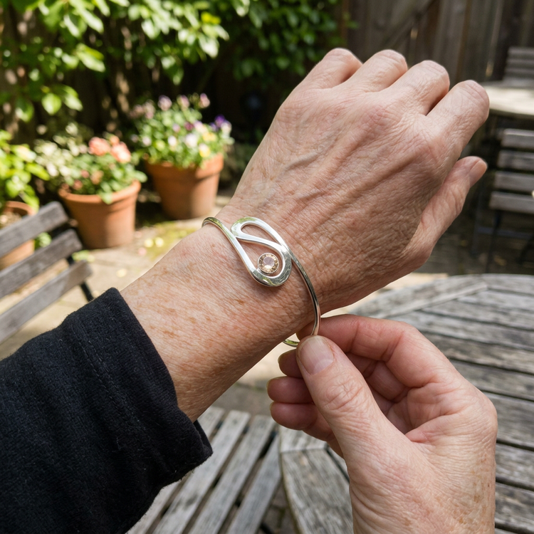 Person adjusting the 'Ebb & Flow' sunstone cuff bracelet in a cozy outdoor setting, highlighting its elegant details and natural colors.