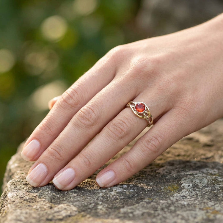 Close portrait of a model in natural light, showcasing her hand adorned with a detailed Oregon Sunstone ring in a peaceful outdoor setting.