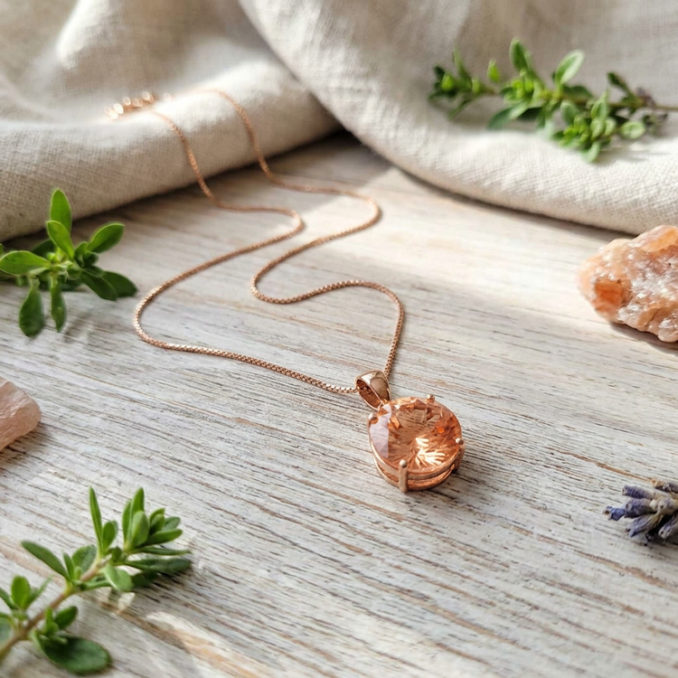 Casual display of a Peach Oregon Sunstone necklace on a light wooden surface with natural elements, emphasizing warm hue and micro-faceted brilliance.