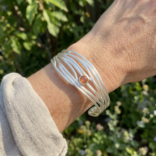 Worn on a model's wrist, the Serene bracelet showcases its tapering sterling silver design with natural outdoor garden background.