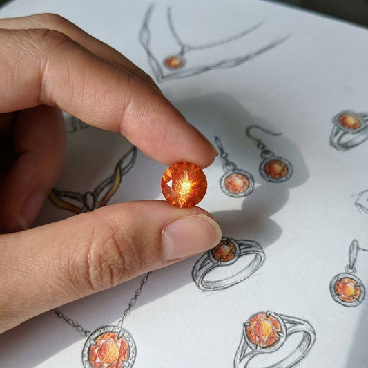 Close-up of a 2.80-carat Oregon Sunstone with sunset orange schiller, held delicately to highlight its vibrant orange color and internal copper particles.