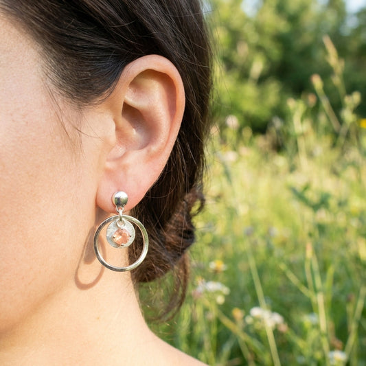 Model wearing Sunstar earrings on ear in outdoor grassy setting, showcasing movement and warm sunstone glow in natural sunlight.