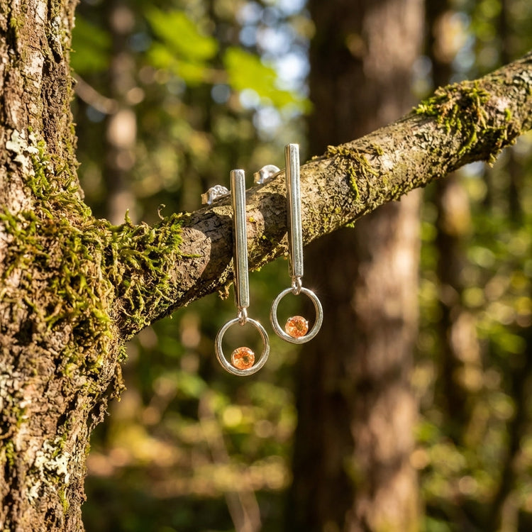 Close-up of Sunstone Dangle Earring hanging from a tree branch in a forest, showcasing craftsmanship and natural beauty.
