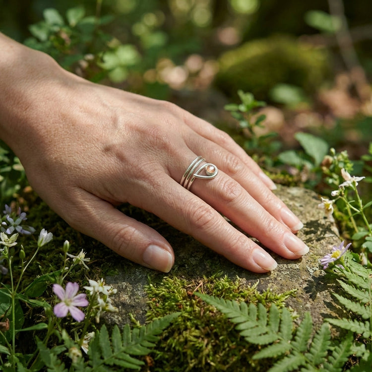 Full-body view of a hand wearing an adjustable Oregon Sunstone ring, outdoors with moss and wildflowers, showcasing casual elegance.