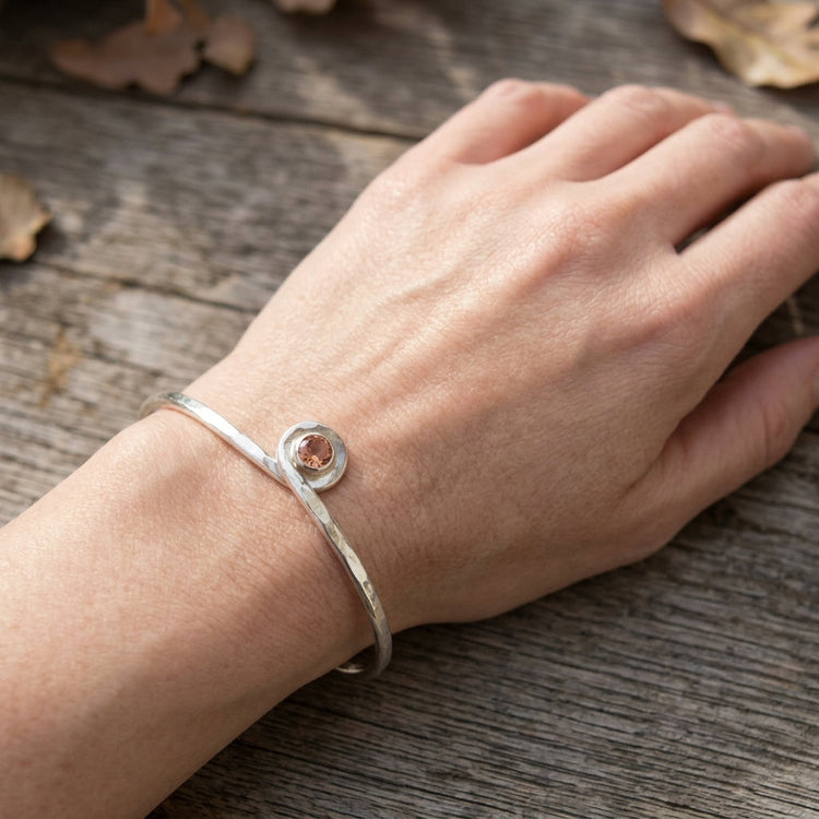 Artistic shot of a hand wearing a silver Oregon Sunstone cuff bracelet against a rustic wooden background, emphasizing craftsmanship and warm sunstone tones.