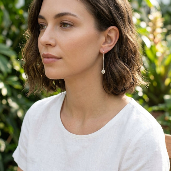 Artistic overhead view of hand with silver ring and subtle silver Sunstone earring in sunny botanical garden.