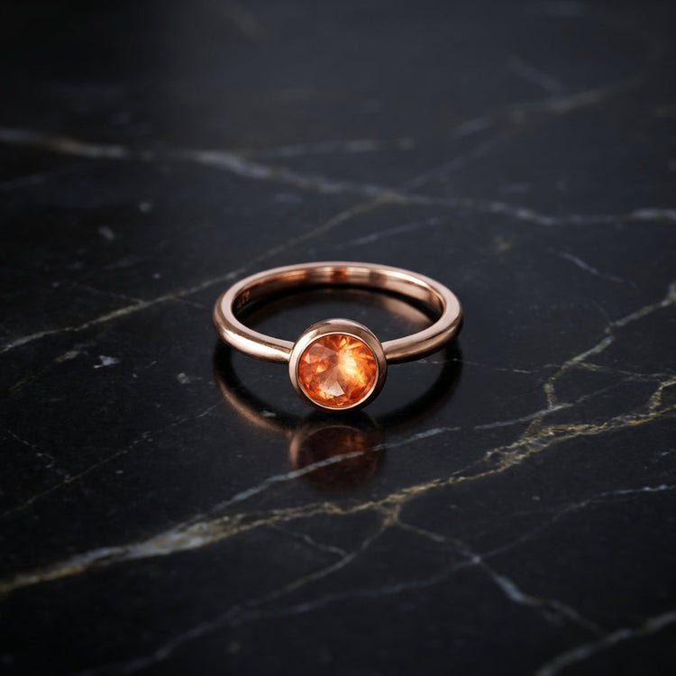 Overhead artistic shot of a rose gold sunstone ring on dark marble, emphasizing its warm glow, micro-texture, and modern elegance under soft lighting.