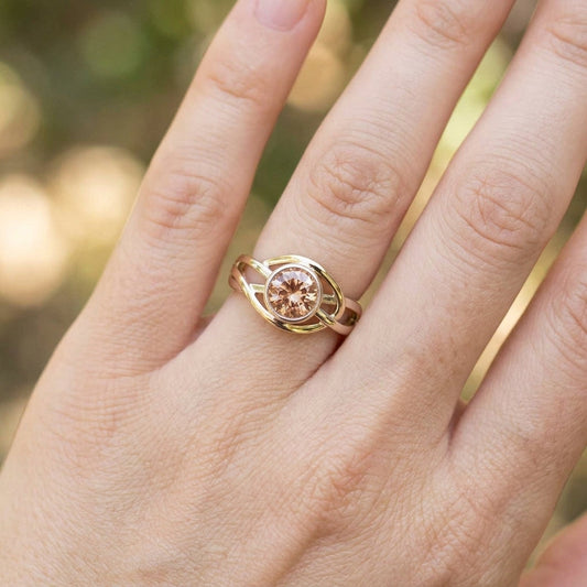 Overhead view of a hand holding a Celtic-inspired Oregon Sunstone ring, with earth-toned background and sharp focus highlighting intricate details.