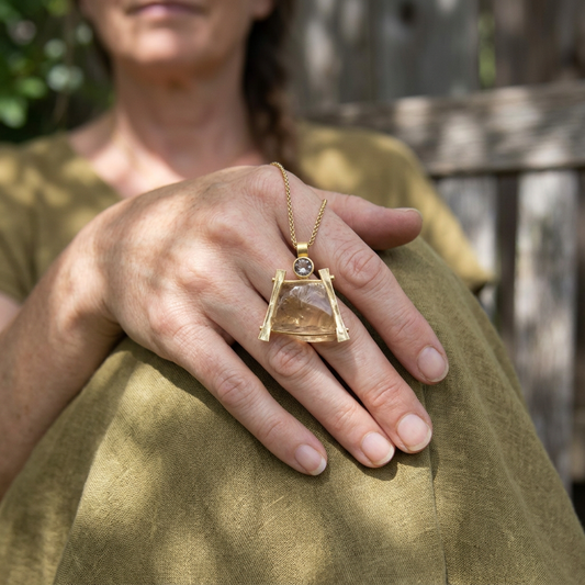 Close-up of a model wearing an 18K gold Zen Pendant with Oregon Sunstone crystal, outdoors with sunlight and greenery.