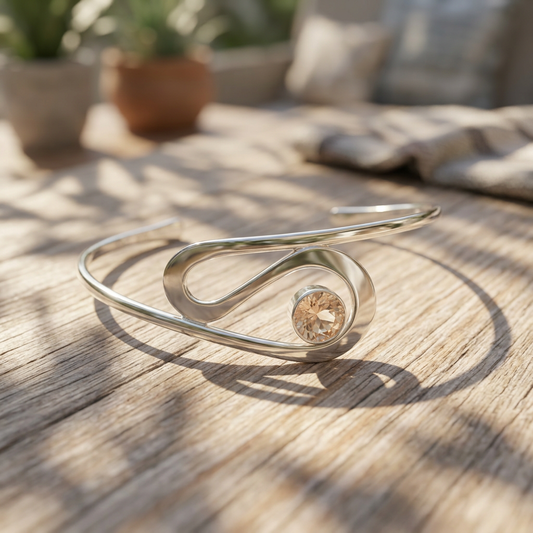 Close-up of the 'Ebb & Flow' double sunstone cuff bracelet on a light wood background, highlighting sterling silver polish and warm sunstone hues.