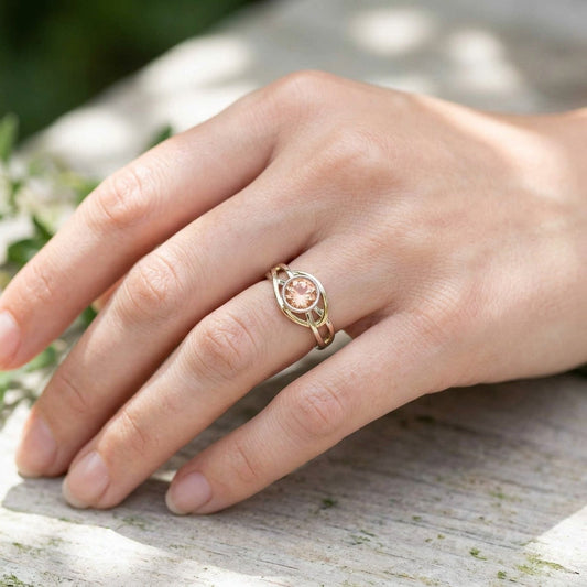 Close-up of a hand wearing a delicate Celtic-inspired Oregon Sunstone ring set in 14K gold with natural outdoor lighting.
