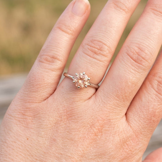 Detailed close-up of a hand with a small Oregon Sunstone 'Starburst' ring, emphasizing craftsmanship and hues against a natural background.