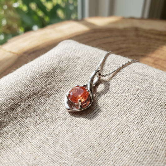 Macro shot of white gold infinity necklace pendant with 8mm bright red sunstone, showcasing micro-textures and natural daylight setting.