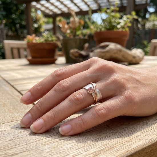 Close-up of manicured hand with Alya Star Sunstone Ring on a wooden surface under natural light, showing intricate details and sparkle.