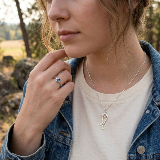 Close-up of model’s neck and hand highlighting the petite Sterling Silver 'Ebb & Flow' necklace with peach Oregon Sunstone pendant.