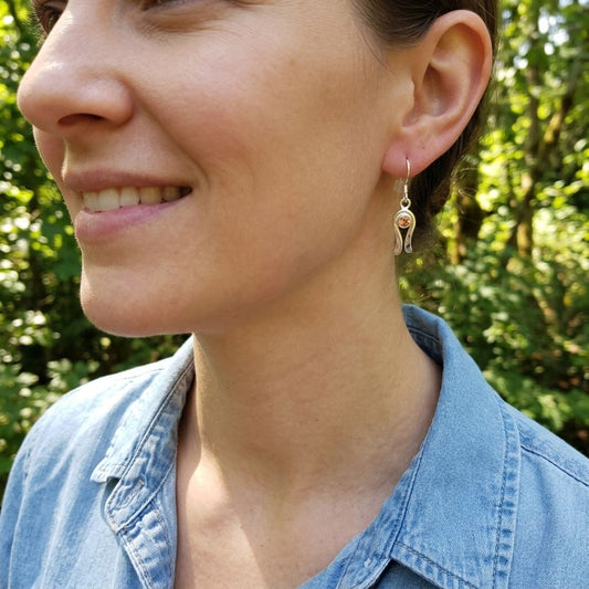 Close-up of a female model wearing delicate silver dangle earrings with peach Oregon Sunstone in natural sunlight.