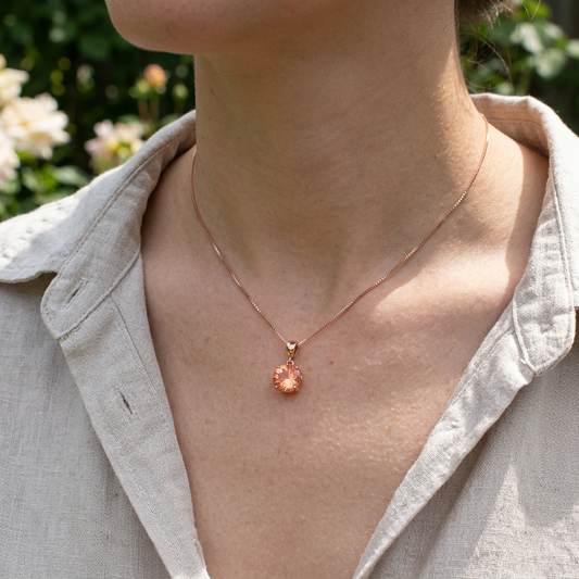 Close-up of a model wearing an Oregon Sunstone pendant on a chain in a natural outdoor setting, showcasing warmth, sparkle, and micro-texture.
