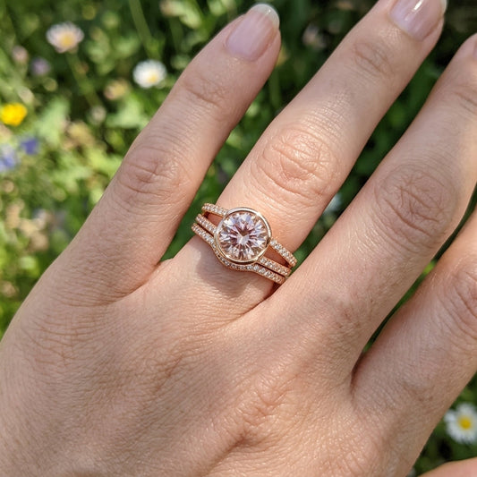 Close-up of a detailed rose gold engagement ring with Oregon Sunstone on a model's hand against a natural outdoor background.