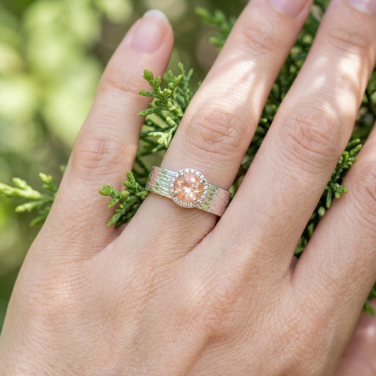 Close-up of Silver 'Ashera Juniper Goddess' ring on a hand holding greenery, emphasizing fine textures and gemstone brilliance.