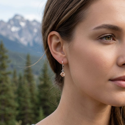 Close-up of a delicate silver sunstone dangle ring on a hand with a natural outdoor background and pine trees, highlighting gemstone clarity and fine details.