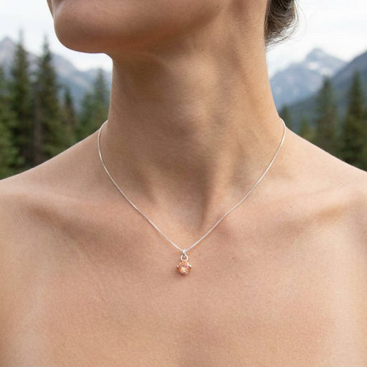 Close-up of a delicate silver Sunstone pendant necklace with chain against a natural wooden background, highlighting the gemstone's shimmer and fine design.