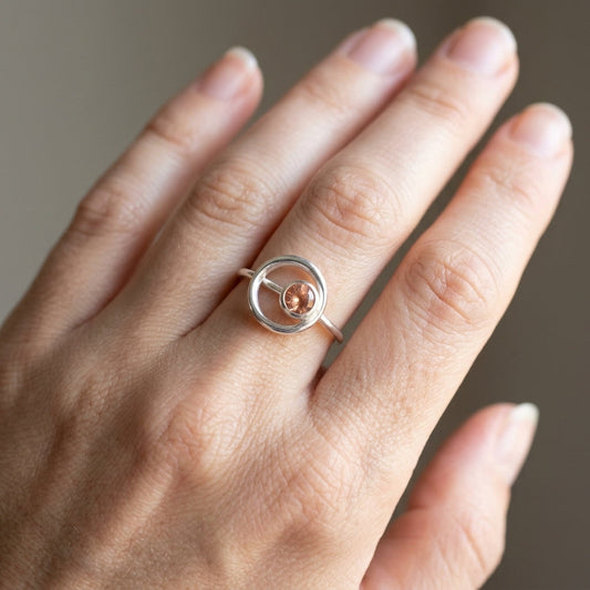 Close-up of delicate sterling silver Orbit Ring set with Oregon Sunstone, displayed on an elegant hand with natural lighting highlighting gemstone's subtle color.