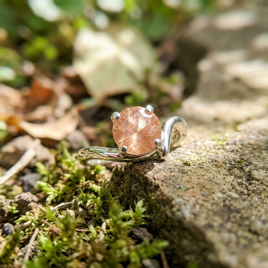 Delicate Oregon Sunstone Solitaire Ring on a silver band with natural outdoor lighting highlighting warm peach shimmer and fine craftsmanship.