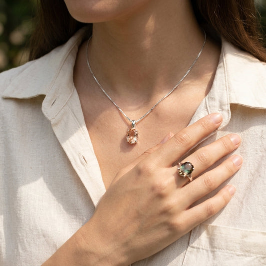 Close-up of a hand holding a gemstone ring with rich color and internal schiller sparkle, natural background.